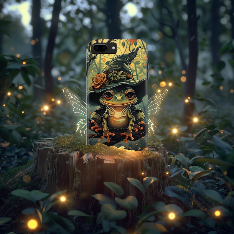 May include: A green frog wearing a witch's hat with a red flower on it. The frog is sitting on a branch with a fairy wing design behind it. The image is on a phone case.