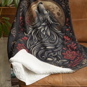 May include: A black and gold throw blanket featuring a detailed illustration of a wolf howling at the moon. The wolf is surrounded by red flowers and intricate floral designs. The background is a dark brown colour.