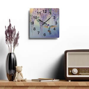 May include: Square clock with a hummingbird flying through purple wisteria flowers. The clock face has black numbers and hands against a blue and white background.