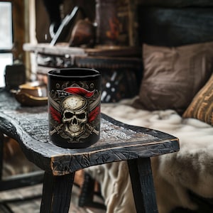 Pode incluir: Caneca de cer&acirc;mica preta com um design de caveira e ossos cruzados. A caveira est&aacute; usando um chap&eacute;u vermelho e branco e tem espadas cruzadas atr&aacute;s.