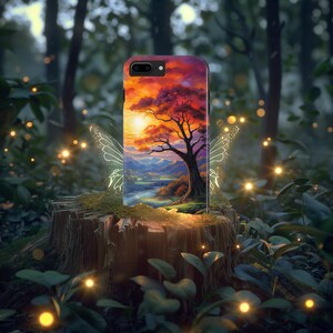 May include: A black iPhone case featuring a colourful sunset landscape with a large tree at its centre. The case is surrounded by fairy wings and glowing lights.