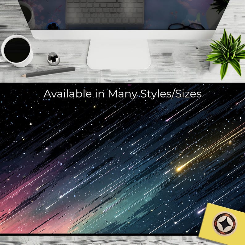 Op de afbeelding: Een zwarte bureaumat met een kosmisch ontwerp van vallende sterren en de tekst "Available in Many Styles/Sizes". Het ontwerp heeft een kleurengradient van blauw, roze en geel, wat een levendige esthetiek cre&euml;ert.