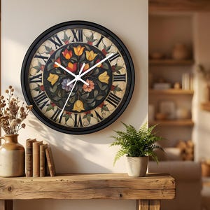 May include: A round wall clock with a black frame and Roman numerals. The clock face features a floral design with yellow, orange, and purple flowers. The clock is mounted on a beige wall. The time is approximately 10:10.