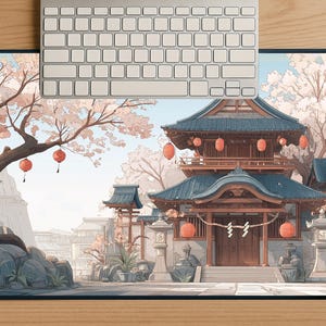以下が含まれることがあります： 青い屋根、赤い提灯、桜の木が描かれた、日本の寺院のイラストが特徴の長方形のマウスパッド。銀色のキーボードがマウスパッドの上に置かれ、木製の表面に置かれています。