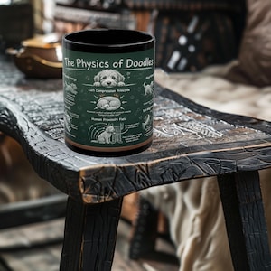 May include: Black ceramic mug with the text "The Physics of Doodles" and diagrams of dogs. The mug features a green background with white illustrations and text. The mug is cylindrical and sits on a wooden surface.