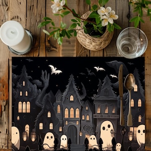 May include: Black and white Halloween themed placemat with a spooky town scene featuring houses, trees, bats, and ghosts. The placemat has a black background and white details.