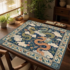 May include: A square game mat featuring a deep blue background with two winding dragons in shades of orange and green, surrounded by white clouds and floral patterns. The border is decorated with a repeating floral motif in blue, green, and tan.