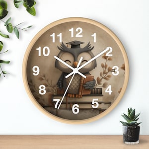 May include: A circular wall clock with a light wood surround. The clock face depicts a cartoon owl in a graduation cap, holding a book, and sitting on books. The clock hands are black, and the numbers are white.