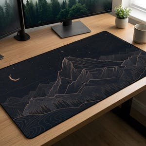 May include: A black desk mat with a mountain scene, a crescent moon, and stars. The mountains are outlined in a copper hue. The mat is rectangular and sits on a wooden desk.