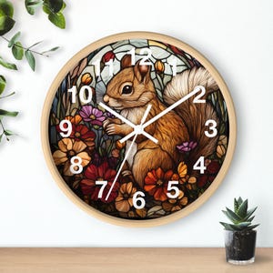 May include: A round wooden wall clock with a white face and black numbers. The clock face features a colorful illustration of a squirrel surrounded by flowers.
