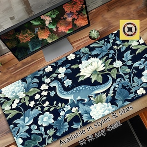 Puede incluir: Una alfombrilla de escritorio con estampado floral azul y blanco con una silueta de dinosaurio. El texto "Disponible en estilos y tamaños para adaptarse a cualquier escritorio" está en la parte inferior de la alfombrilla.