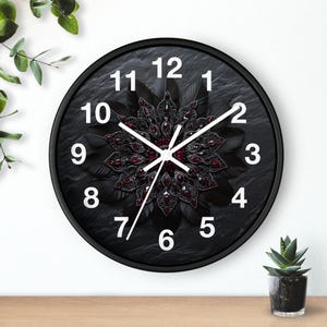 Puede incluir: Reloj negro con un diseño de joyas negras y rojas en el centro. La esfera del reloj tiene números y manecillas blancas.