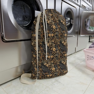 May include: A black laundry bag with a drawstring closure. The bag features a repeating pattern of black birds and yellow flowers on a dark background.
