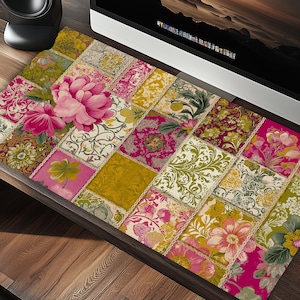 May include: A floral patchwork desk mat featuring a large pink peony and various floral patterns in shades of pink, yellow, green, and cream. The mat is rectangular and designed to sit under a computer monitor.
