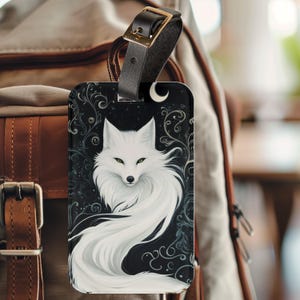 May include: A white fox with a long, flowing tail is depicted on a black background with a crescent moon and swirling floral patterns. The image is printed on a luggage tag.