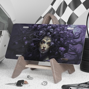 May include: A purple and black license plate featuring a woman with long, flowing hair adorned with skulls. Her eyes are a bright, piercing yellow. The background is a dark, swirling pattern.