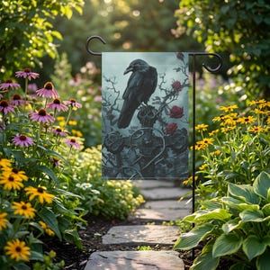 Könnte beinhalten: Eine rechteckige Gartenflagge mit einem schwarzen Raben, der auf einem verwitterten Steinkreuz sitzt. Das Motiv zeigt dunkle, dornige Zweige und mehrere tiefrote Rosen vor einem gedämpften, neblig-blaugrauen Hintergrund an einem schwarzen Metallständer.