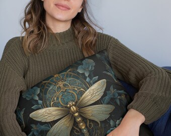 Puede incluir: Una almohada decorativa con un fondo verde oscuro que presenta una libélula dorada y azul con detalles intrincados. La libélula está rodeada de elementos florales y una esfera de reloj.