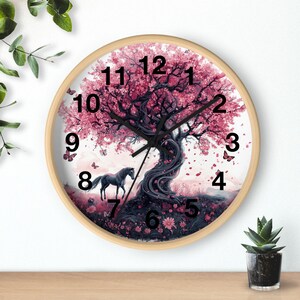 May include: A round wooden wall clock with a white background and a pink and purple tree with a black horse standing in front of it. The clock face has black numbers and hands.