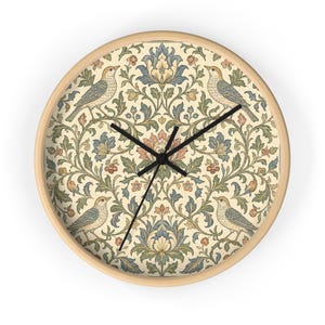 May include: Round wall clock with a light wood frame. The clock face features a cream-colored background with a floral and bird pattern in blue, green, and peach tones. Black clock hands indicate the time.