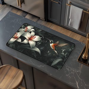 May include: A black and white mouse mat featuring a hummingbird and white lilies against a dark background. The hummingbird is in flight with its wings outstretched. The lilies are in full bloom, with white petals and red centres.