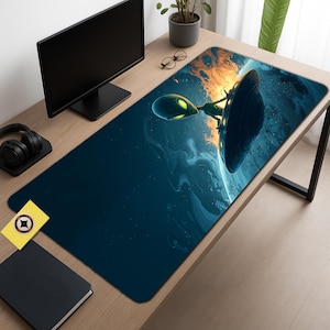May include: A rectangular desk mat featuring a vibrant illustration of an alien and a spaceship against a cosmic background. The design incorporates shades of blue, orange, and green. The mat is placed on a wooden desk, alongside a computer monitor and other office accessories.