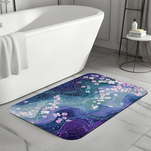 Könnte beinhalten: Eine blaue und violette Badematte mit einem weißen und rosa Blumendesign. Die Matte hat ein wirbelndes, abstraktes Muster.