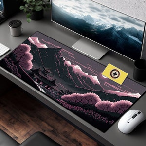 May include: A black and pink mousepad with a Japanese-inspired design featuring a mountain range, a temple, and cherry blossoms. The mousepad is on a gray desk with a computer monitor, a mouse, and a yellow card with a star.