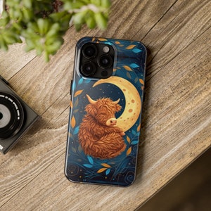 May include: A phone case featuring a charming cartoon Highland cow napping on a crescent moon. The background is a dark blue with stars and a floral pattern.