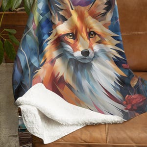 May include: A soft, plush throw blanket featuring a colorful, abstract illustration of a fox's face. The fox has a red-orange coat and blue eyes. The background is a mix of blue, purple, and green hues.