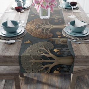 May include: A dark teal table runner featuring a detailed illustration of two trees with gold-colored leaves and branches. The runner is set on a wooden table with place settings, wine glasses, and a vase of pink flowers.