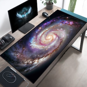 May include: A large galaxy-themed mousepad with a swirling nebula design in shades of purple, pink, orange, and white. The mousepad is on a wooden desk with a computer monitor and other office supplies.