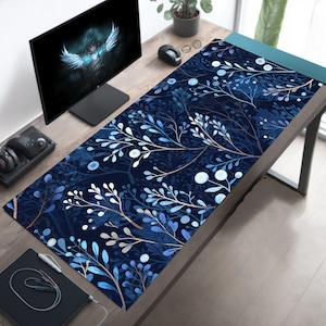 May include: A blue and white floral patterned desk mat with a dark blue background. The mat is on a wooden desk with a computer monitor, a mouse, and a plant.