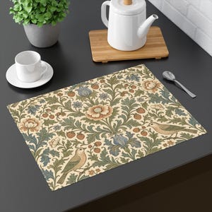 May include: A rectangular placemat featuring a repeating pattern of beige flowers, blue iris-like blooms, green foliage, and small red strawberries, with two birds perched among the stems on a cream-colored background.