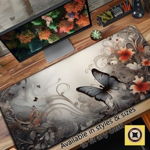May include: A gray and white desk mat with a large butterfly design. The butterfly is gray with black markings and is surrounded by swirling floral patterns. The text "Available in styles & sizes to fit any desk" is printed on the mat.