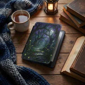 May include: An e-reader with a cover featuring a fantasy forest scene with a stone path, glowing lights, and purple foliage. A cup of tea, a lantern, a scarf, and books are arranged on a wooden surface.