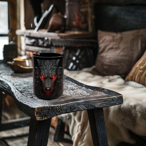 May include: Black ceramic coffee mug featuring a wolf's face design. The wolf has glowing red eyes and a fierce expression.