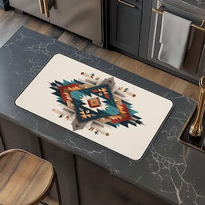 May include: Rectangular kitchen mat with a cream background and a geometric design in shades of teal, orange, brown, and grey. The design has a Native American inspired pattern. The mat has a black border and is placed on a dark countertop.