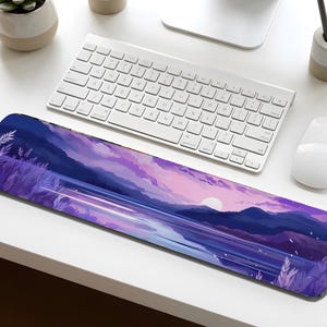 May include: A rectangular desk mat featuring a landscape design with a sunset over a lake and mountains. The color palette includes shades of purple, blue, and pink. A white keyboard and mouse are also visible.