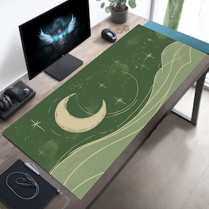 Puede incluir: Una alfombrilla de ratón verde y beige con un diseño de luna creciente y un sutil patrón de ondas. La alfombrilla de ratón tiene un tema de cielo estrellado con estrellas blancas.