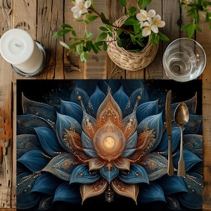 Può includere: Un sottopiatto decorativo con un elaborato motivo floreale blu e oro. Il sottopiatto presenta un elemento centrale dorato brillante, con un coltello e un cucchiaio a destra. Sono visibili anche una candela, un bicchiere e una piccola pianta.