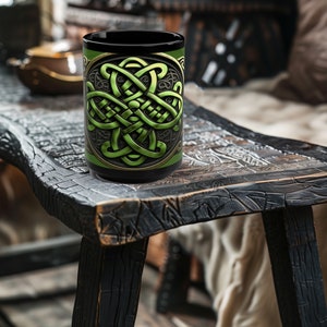 May include: A black ceramic mug with a green Celtic knot design. The mug is sitting on a dark wooden table.