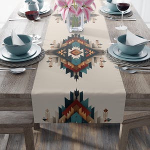 May include: A beige table runner with a geometric Southwestern design in shades of teal, rust, and tan. The runner is placed on a wooden table set for a meal, with plates, bowls, silverware, and wine glasses.