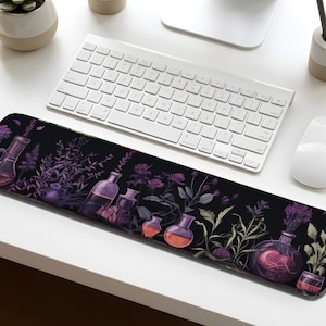 May include: A black desk mat featuring a botanical design with purple and orange potion bottles and various plants. The mat is rectangular and sits beneath a white keyboard and mouse.