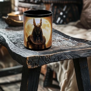 May include: Black ceramic coffee mug with a full moon and an image of the Egyptian god Anubis with a golden headdress.