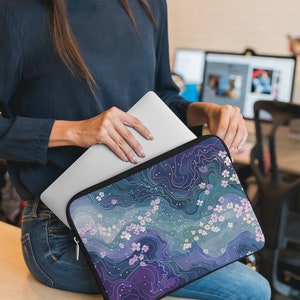 May include: A laptop sleeve with a zipper closure. The sleeve has a blue, purple, and white abstract design with white flowers.