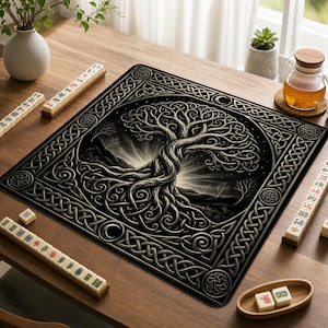 May include: A square game mat featuring a central black and white illustration of a tree with intricate, swirling knotwork branches and roots. The mat is bordered by a geometric Celtic knot pattern and is surrounded by several mahjong tiles.