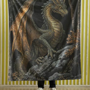 Pu&ograve; includere: Una coperta in pile nero con un drago verde scuro e marrone con grandi ali. Il drago &egrave; appollaiato su una scogliera rocciosa con uno sfondo di foresta oscura.