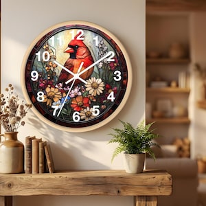 May include: Round wall clock with a stained glass design featuring a red cardinal bird perched among colorful flowers. The clock has a light wood frame and white numerals. The clock hands are white.