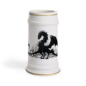 May include: White ceramic beer stein with a black silhouette of a dragon with red eyes. The dragon is surrounded by vines and a castle in the background.